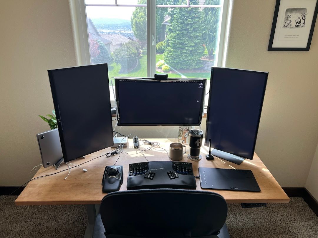 My desk setup in 2024, including a Macbook Pro, three 4K monitors, and various input devices.